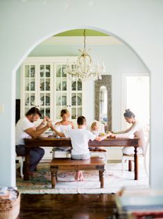 a group of people sitting around a wooden table in a living room next to a doorway