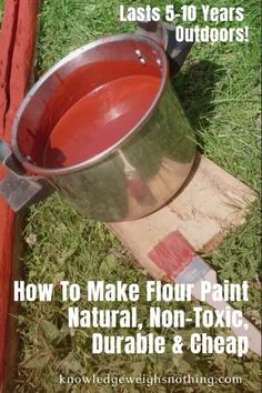 a metal bucket sitting on top of a wooden block next to grass and red paint