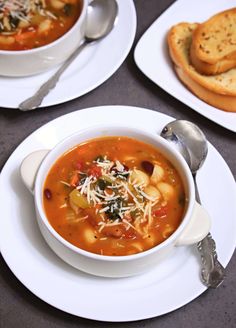 two bowls of soup on plates with silver spoons next to bread and crackers