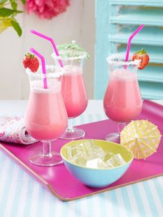 two glasses filled with pink liquid and strawberries on top of a tray next to an umbrella