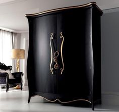 a black armoire with gold accents in a living room area next to a chair