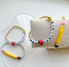 three bracelets are sitting next to each other on a white surface, one is yellow and the other is red