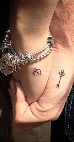 two people holding hands with tattoos on their wrists and one has a key to each other