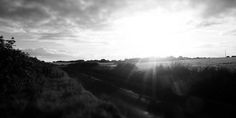 the sun shines brightly through the clouds over an empty train track in black and white