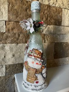 a bottle with a snowman on it sitting on top of a shelf next to a stone wall