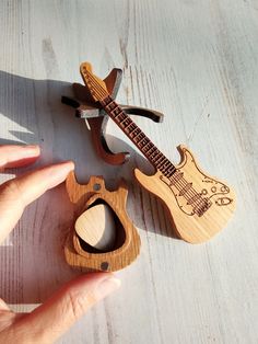 a hand holding a wooden toy guitar next to another one with a hole in it