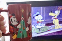 a person holding a coffee mug in front of a television with mickey mouse on it