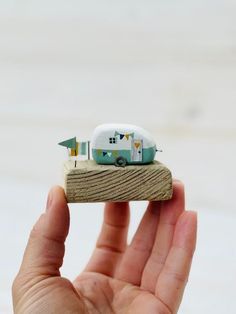 a hand holding a tiny toy camper on top of a piece of wood