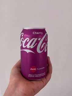 a hand holding a can of coca - cola in front of a white wall with the words cherry cola on it