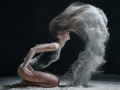 a woman kneeling on the ground with her hair blowing in the wind and dust behind her