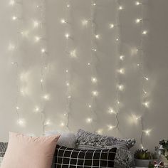 a bed with white lights on the wall above it and pillows in front of it