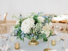 a centerpiece with white and blue flowers sits on top of a round table at a wedding reception