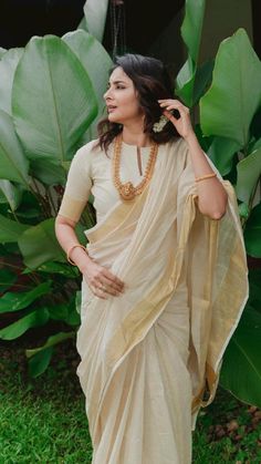 a woman in a white sari standing next to some green plants and greenery