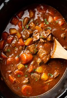 beef stew with carrots, potatoes and parsley in a slow cooker being stirred by a wooden spoon