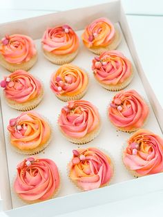 cupcakes with pink and orange frosting in a white box on a table