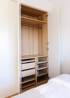 an empty bedroom with white linens and wooden shelves on the wall next to a bed