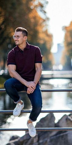 a man sitting on a rail next to a body of water with trees in the background