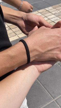 two people are holding hands on the street and one person is wearing a black bracelet