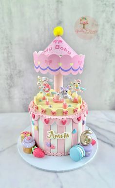 a pink and yellow carousel cake with cupcakes on the table next to it