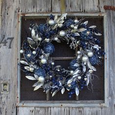 a wreath with blue and silver decorations hanging on an old wooden door, in front of a brick wall