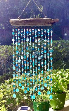 a wind chime hanging from a tree in the garden with potted plants and flowers