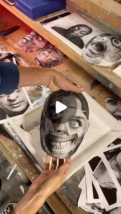 a person holding up a skull mask in front of some pictures on a table with scissors