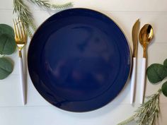 a blue plate sitting on top of a table next to silverware and greenery