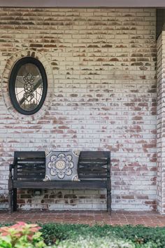 a bench sitting in front of a brick wall with a circular window on the side