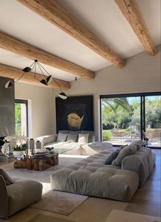 a living room filled with lots of furniture next to large windows and wooden beams