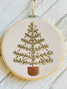 a small embroidered christmas tree in a pot on a white wooden surface with a string hanging from the hoop