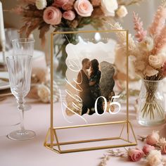 a table topped with a glass vase filled with flowers and a photo frame on top of it