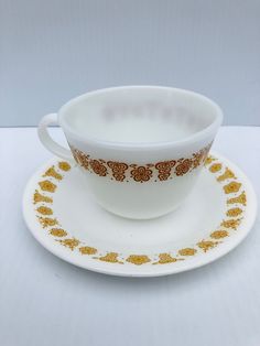 a white cup and saucer with gold designs on the rim, sitting on a plate