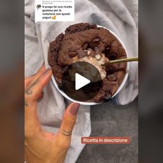 a person holding a bowl of ice cream with chocolate chips and cookies in it on top of a white cloth