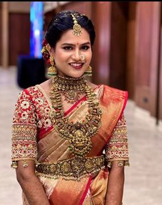 a woman in a red and gold sari with jewelry on her neck smiling at the camera