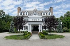 a large white house with lots of trees and bushes around it's front entrance