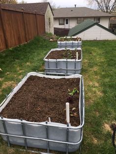 three metal containers filled with dirt and plants in the grass next to a fenced yard