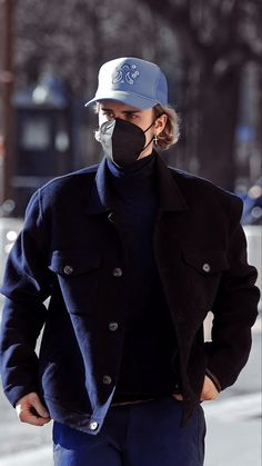 a man wearing a face mask while walking down the street with his hands in his pockets