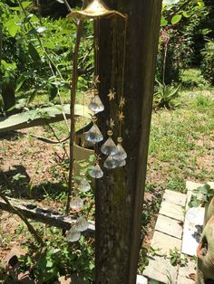 an outdoor light hanging from the side of a wooden pole in a garden with green plants