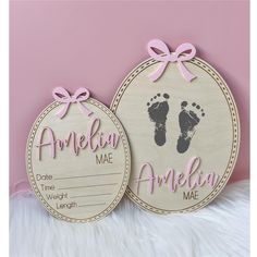 two personalized wooden tags with baby footprints and pink bows on them, one is for the