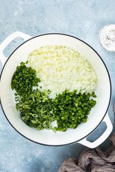 rice and green onions in a white pot on a blue surface with a cloth next to it