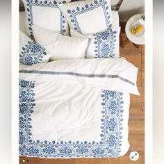 a bed with white and blue comforters on top of it next to a table