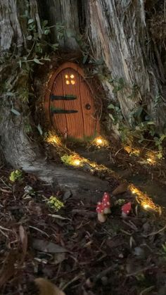 a fairy door in the middle of a tree with lights around it and mushrooms on the ground