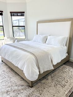 a large bed sitting in the middle of a bedroom next to two windows and a rug