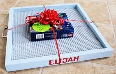 a lego box wrapped in red ribbon and tied with a bow on the lid, sitting on a tile floor