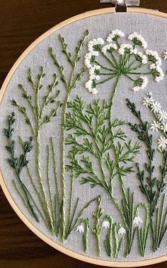 a close up of a embroidery on a piece of cloth with white flowers and green leaves