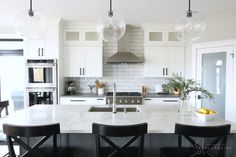 a kitchen with marble counter tops and black chairs in front of an island that has three pendant lights hanging from the ceiling