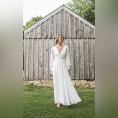 a woman wearing a white dress standing in front of a wooden building with grass and trees