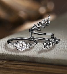 three rings with diamonds on them sitting on top of a cloth covered table next to a book