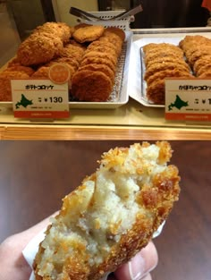 a person holding up a piece of food in front of some trays with pastries