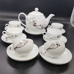 a table topped with white dishes filled with cups and saucers next to a vase